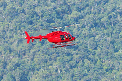A helicopter hovering over a green forest landscape.