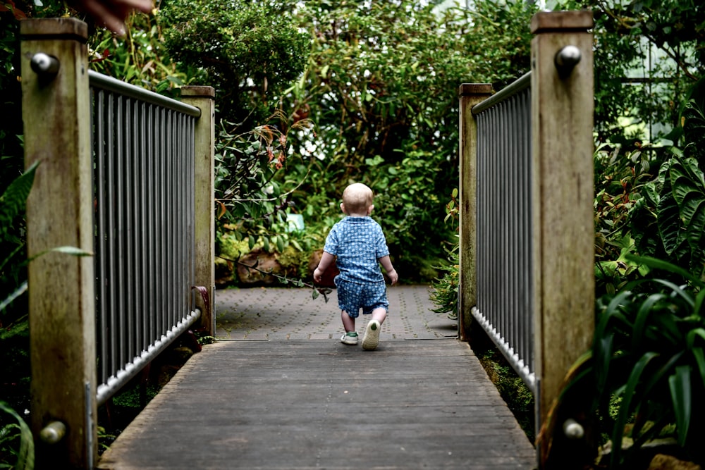 a little boy walking across a wooden bridge