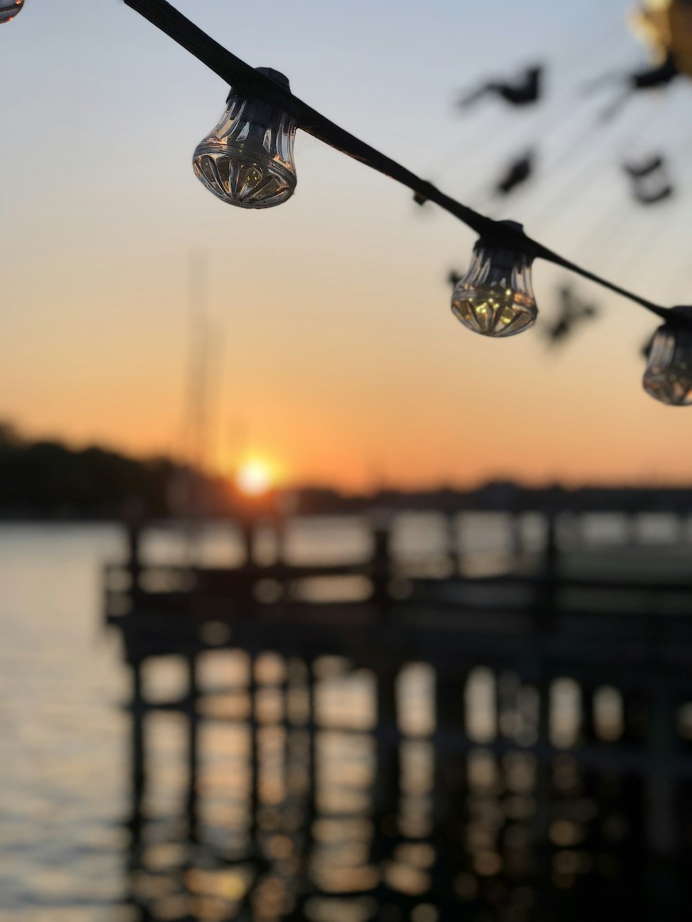 the sun is setting over the water and some lights