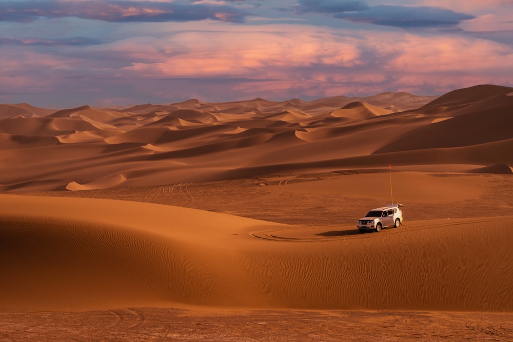 a truck driving through the desert with sand dunes in the background