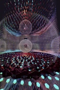 A mesmerizing digital artwork featuring intricate geometric patterns with three large spherical structures at the center. The spheres appear to be composed of thin, transparent meshes surrounded by a vast array of glimmering, faceted elements reminiscent of crystalline forms. The scene is set within a reflective environment that amplifies the complexity and beauty of the design.