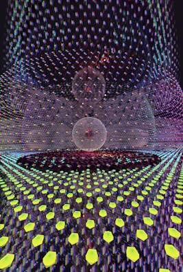 A visually complex scene featuring a symmetrical pattern with a central spherical object overlaid with a grid of glowing hexagonal shapes. The spherical object appears to be composed of intersecting lines, creating a wireframe look. The background is filled with a vibrant array of colors and reflections, giving a sense of depth and digital texture.
