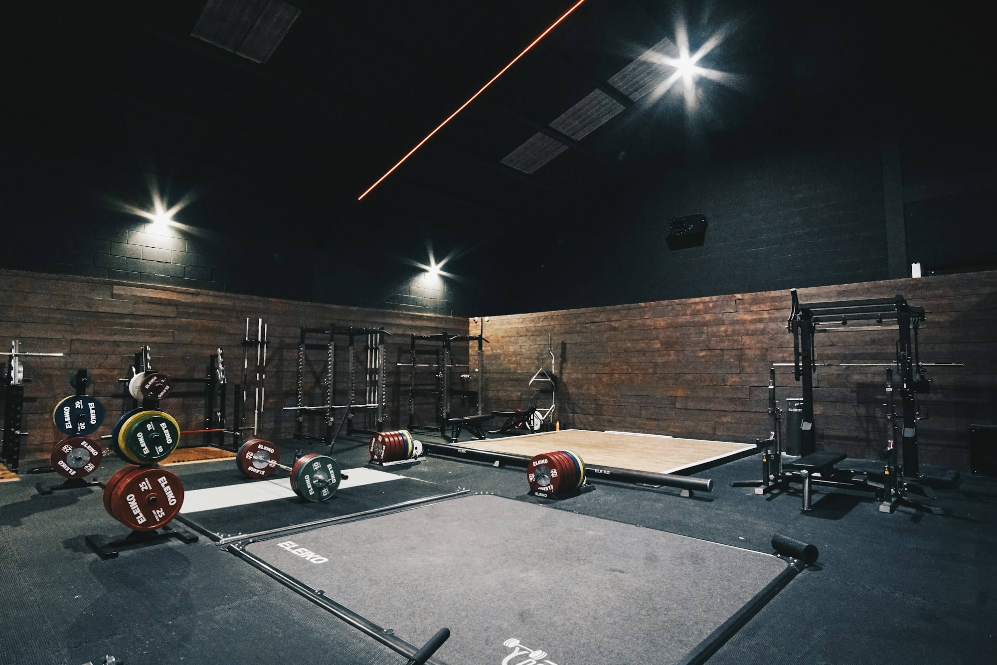 Dark lifting hall with deadlift platforms, loaded bars and wood walls under spot lighting