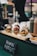 Three gourmet vegan burgers are artfully arranged on a wooden serving board. Each burger is topped with a variety of colorful vegetables and sauces. The buns have a rustic look, with seeds visible on the surface. In the background, several condiment bottles are placed, suggesting a food stall or a street food setting. A small sign in front reads 'Vegan Burgers', indicating that these are plant-based options.