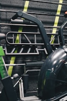 A gym setting with various gym equipment, including bars and handles hanging on a wall. The background is adorned with neon green diagonal stripes on a textured black brick surface.