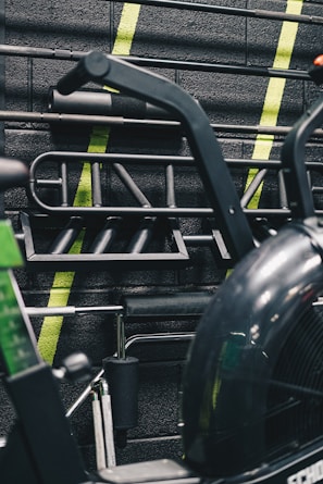 A gym setting with various gym equipment, including bars and handles hanging on a wall. The background is adorned with neon green diagonal stripes on a textured black brick surface.