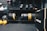 A gym setting featuring various fitness equipment, including kettlebells, stacked weight plates on a rack, dumbbells, and a medicine ball. The gym has a rugged, industrial vibe with black walls and a Bulldog Gear plyo box.
