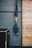 A pair of black and yellow suspension training straps hang from a sturdy metal support against a dark gray textured wall. A wooden panelled section is adjacent, with a black exercise box positioned on the floor.
