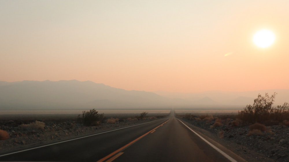 the sun is setting over a desert road