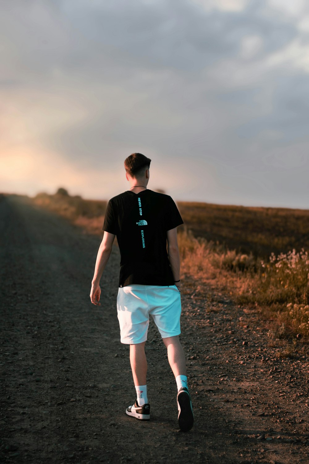 a man walking down a dirt road with a cross on his shirt