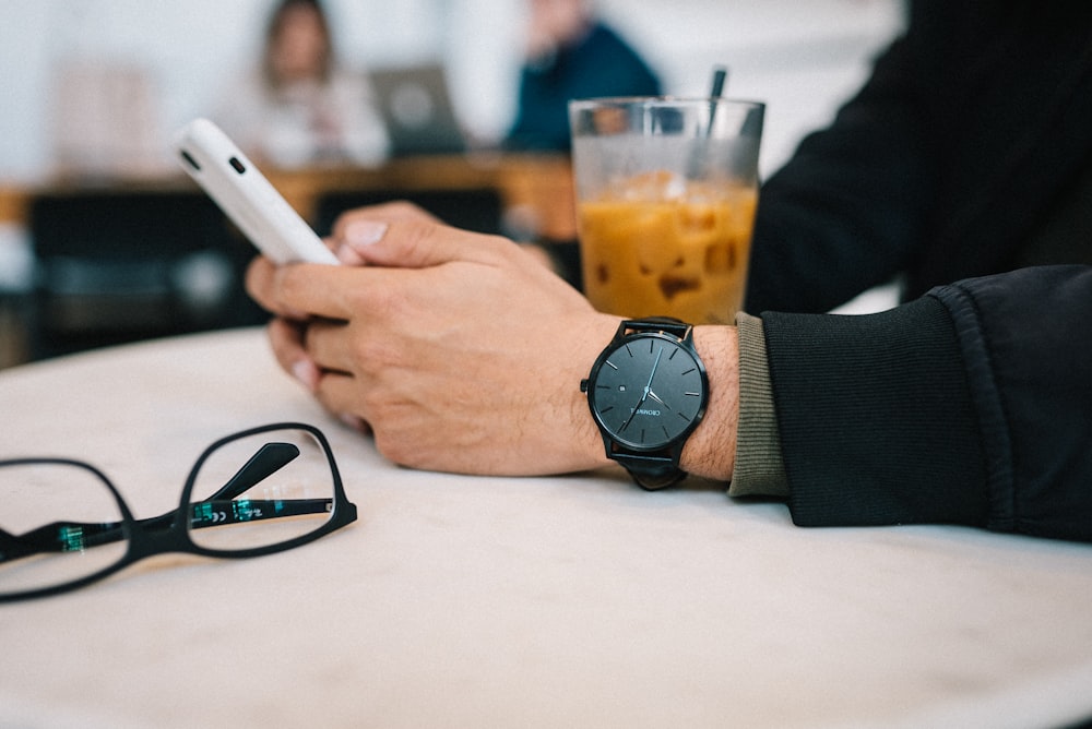 um homem sentado em uma mesa segurando um telefone inteligente