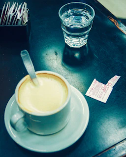 A steaming cup of black coffee next to a small bowl of sugar cubes and a spoon