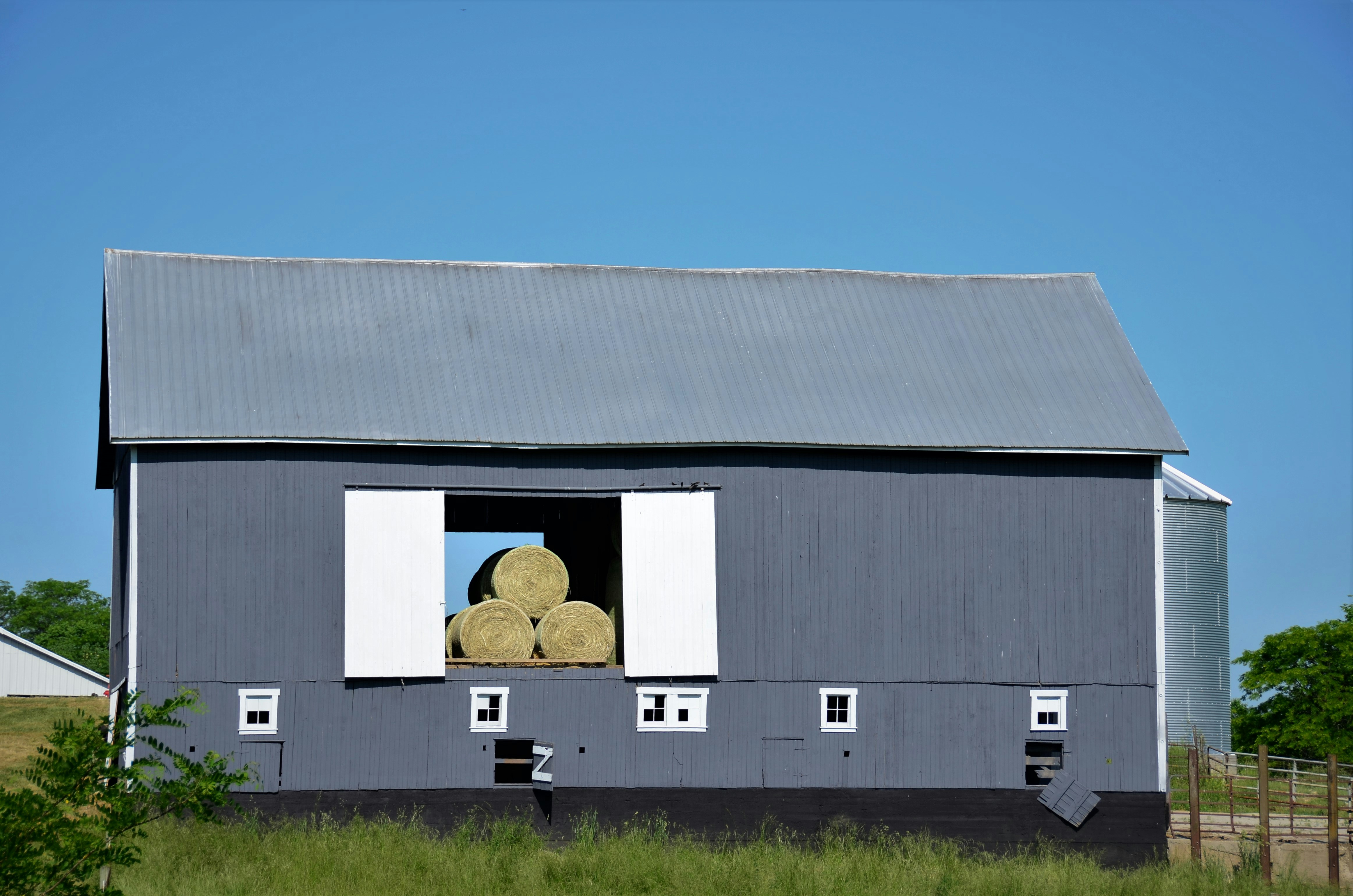 Gray barn with white trim and hay rolls