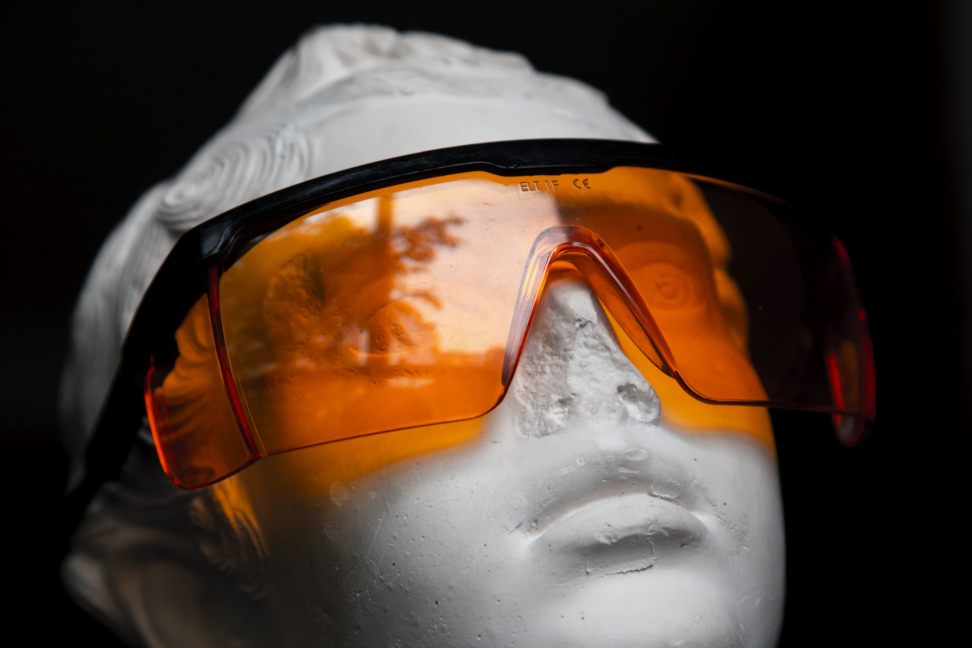 A plaster bust (a statue head, not a real person) wearing orange protective safety glasses (stand-in for IPL eye protection)
