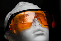 A plaster bust (a statue head, not a real person) wearing orange protective safety glasses (stand-in for IPL eye protection)