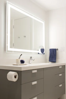 Modern white vanity with black countertop and integrated smart mirror glowing gently.