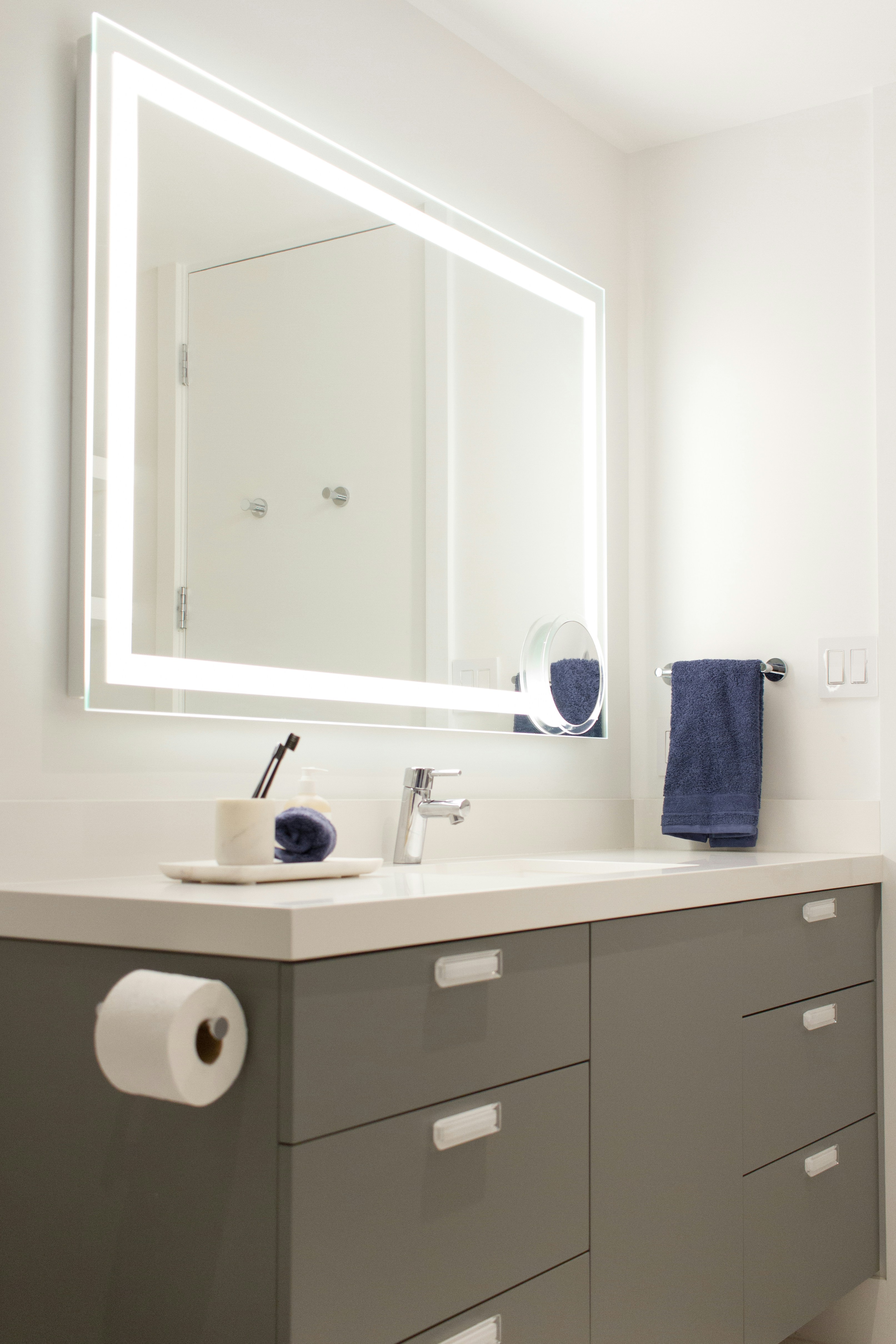 A pristine white bathroom featuring an illuminating mirror that enhances the ambiance. The towel and brush holders offer practicality while harmonizing with the overall aesthetic.