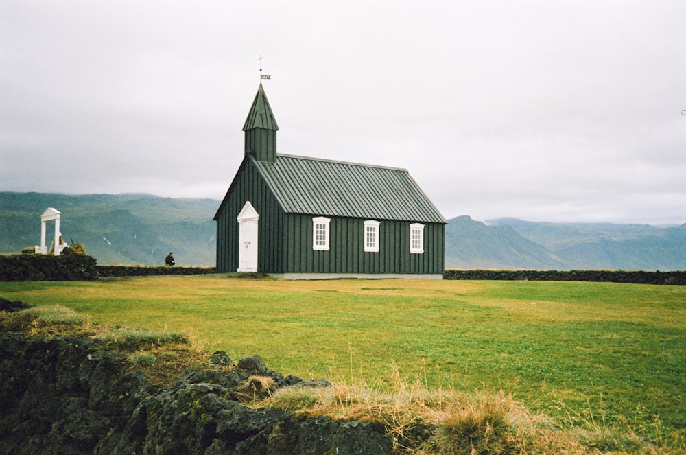 a green church with a steeple on a grassy hill