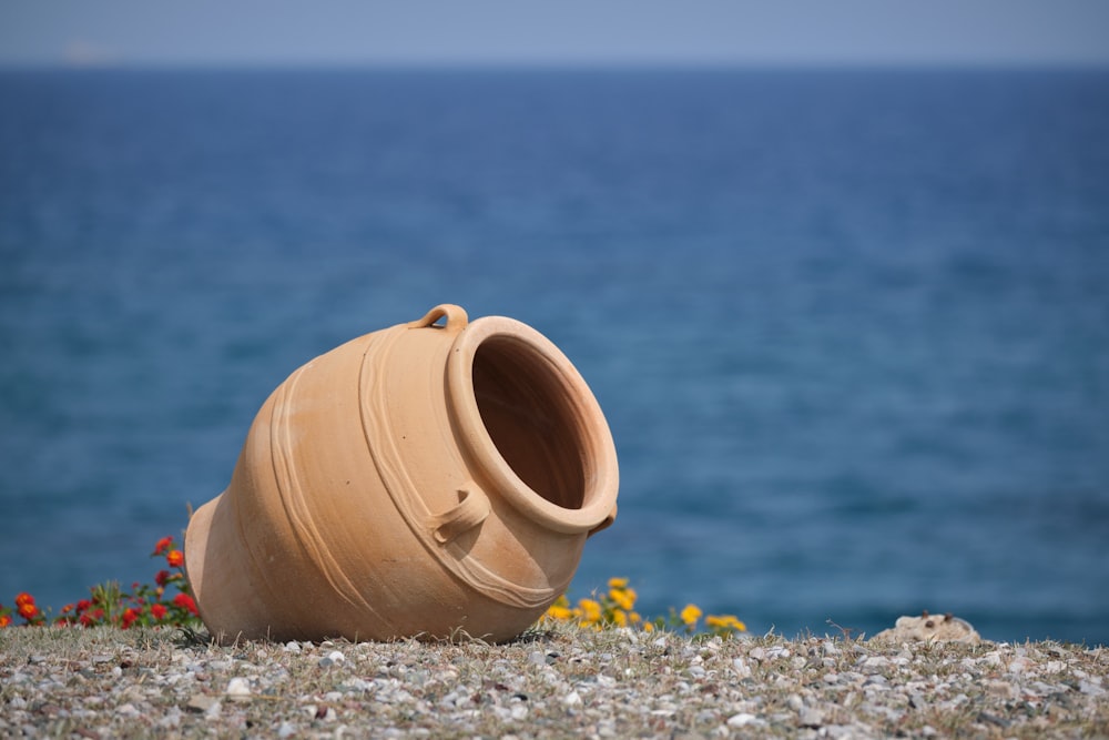 a clay pot sitting on the ground next to a body of water