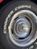 Close-up of a car tire with the words 'COOPER COBRA' prominently displayed in white letters on the black rubber surface. The tire is mounted on a metal rim with intricate, radial design and a shiny, reflective central hubcap.