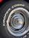 Close-up of a car tire with the words 'COOPER COBRA' prominently displayed in white letters on the black rubber surface. The tire is mounted on a metal rim with intricate, radial design and a shiny, reflective central hubcap.