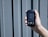 A hand is holding a digital device displaying a reading of 0.3 mmol/L labeled as ketone. The device has a small screen with buttons below it, against a textured, gray, vertical panel background.