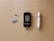 A blood glucose meter is centrally placed on a beige surface, displaying a reading of 103 mg/dL. To its left is a blue lancet for blood sampling, and a black test strip. On the right side is a white and gray lancing device.
