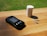 A glucose meter with a digital display reading 103 is placed on a wooden surface. Next to it, there is a small white container and two test strips. Sunlight is casting shadows, creating a relaxed and natural atmosphere.