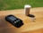 A glucose meter with a digital display reading 103 is placed on a wooden surface. Next to it, there is a small white container and two test strips. Sunlight is casting shadows, creating a relaxed and natural atmosphere.