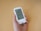 A person holds a white blood glucose meter displaying a reading of 103 mg/dL. The device features a digital screen with additional icons and information.