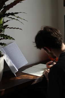 Artistic close-up of hands writing notes on a workbook, surrounded by plants