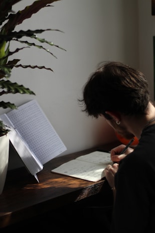 A person writing in a journal surrounded by plants.