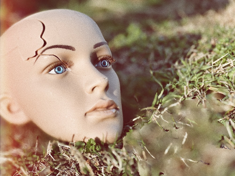 a white mannequin head laying in the grass