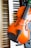 A violin rests on a keyboard, with black and white keys visible beneath the orange-brown body of the violin. Part of an electronic instrument with buttons and dials is also visible.