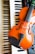 A violin rests on a keyboard, with black and white keys visible beneath the orange-brown body of the violin. Part of an electronic instrument with buttons and dials is also visible.