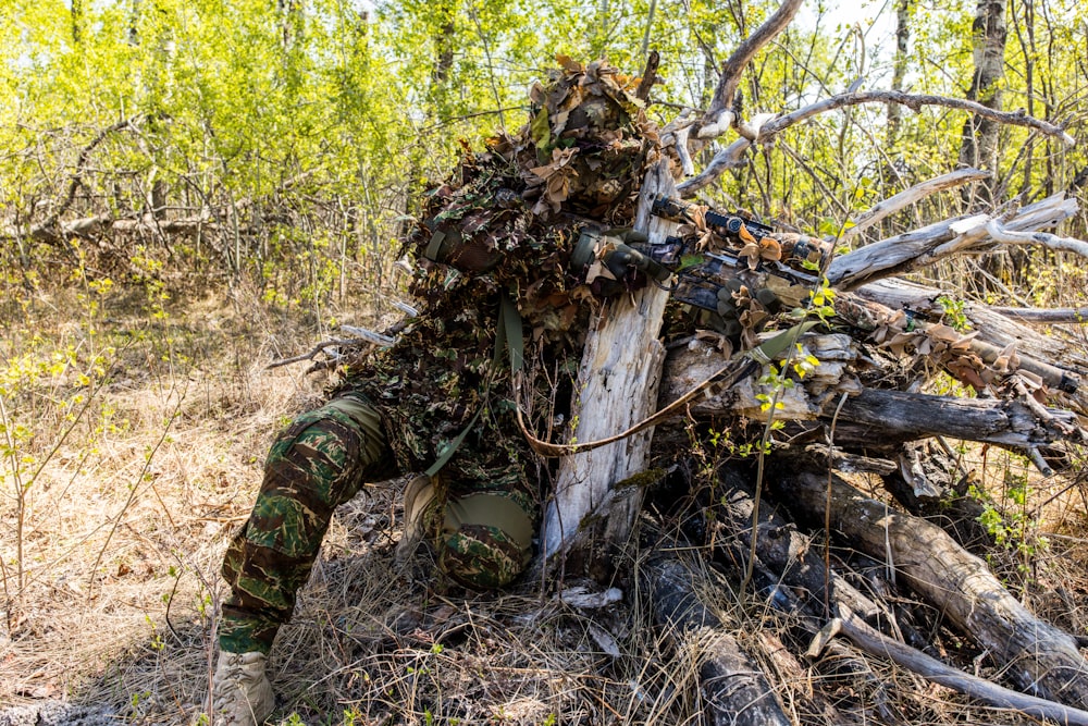 a man in camouflage sitting on top of a tree stump