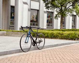 A bicycle with a secure box carrying eyeglasses, parked outside a green urban area.