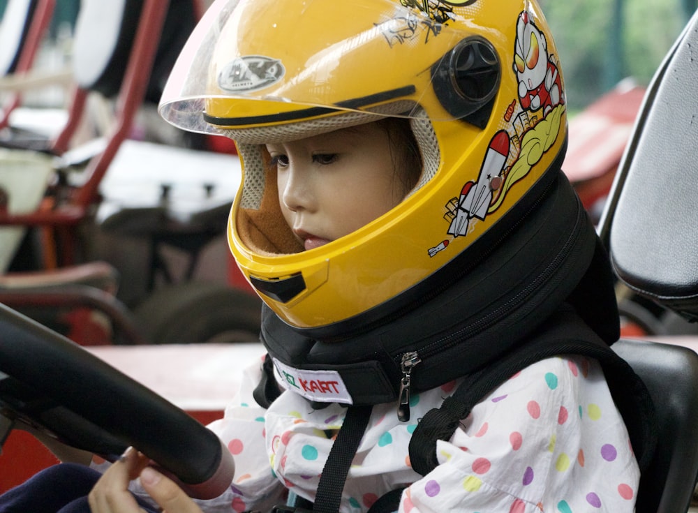 a little girl wearing a yellow helmet and holding a steering wheel