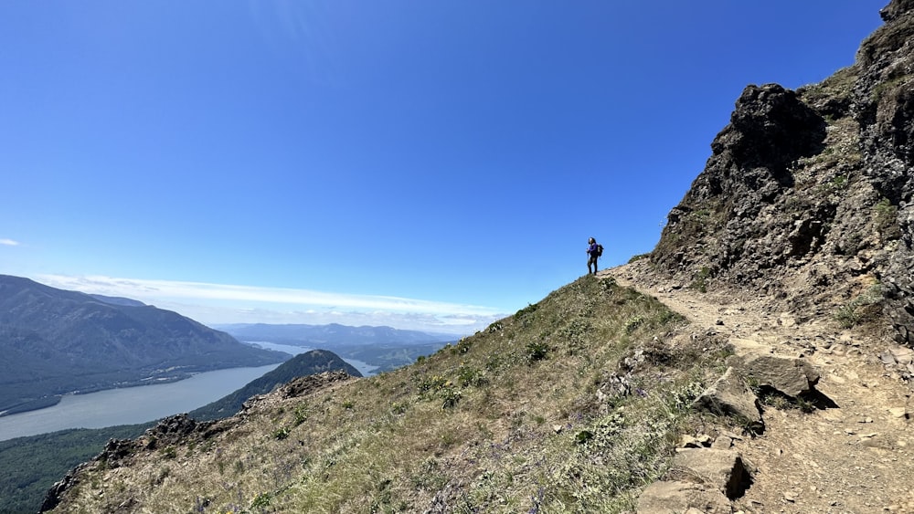 a man standing on top of a mountain next to a lake