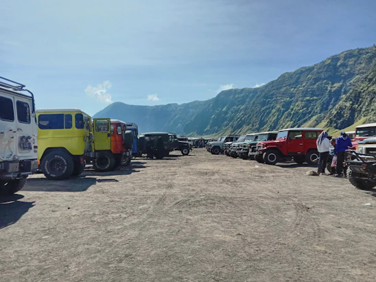 A group of Jeep owners gathered around their vehicles on a rocky trail, sharing laughs and stories under a clear blue sky.
