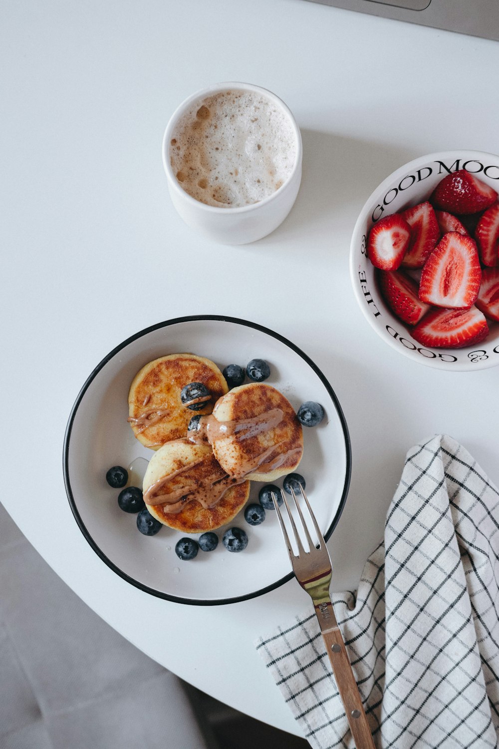 a white table topped with a plate of pancakes and berries