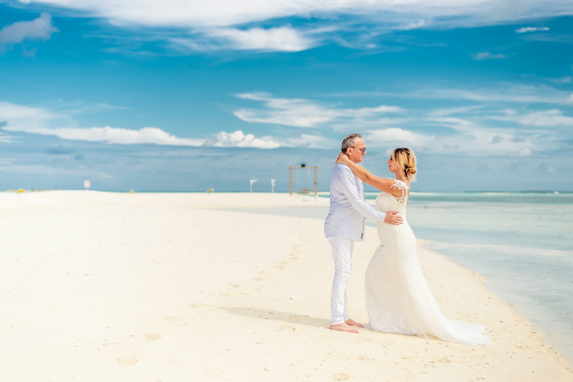 Bride and groom sharing a joyful moment on a sunlit beach in Cádiz, with soft waves in the background.