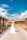 A bride in a white gown stands on a wooden boardwalk beside overwater bungalows. The sky is bright blue with scattered clouds, creating a picturesque tropical setting.