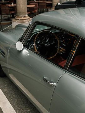 A classic car with a glossy exterior and vintage design is parked next to a row of empty outdoor tables and chairs, creating a serene and nostalgic atmosphere.