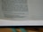 A close-up of a page from an open book. Visible text includes a passage with both narrative content and dialogue. The page has a green bookmark ribbon at the bottom.