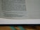 A close-up of a page from an open book. Visible text includes a passage with both narrative content and dialogue. The page has a green bookmark ribbon at the bottom.