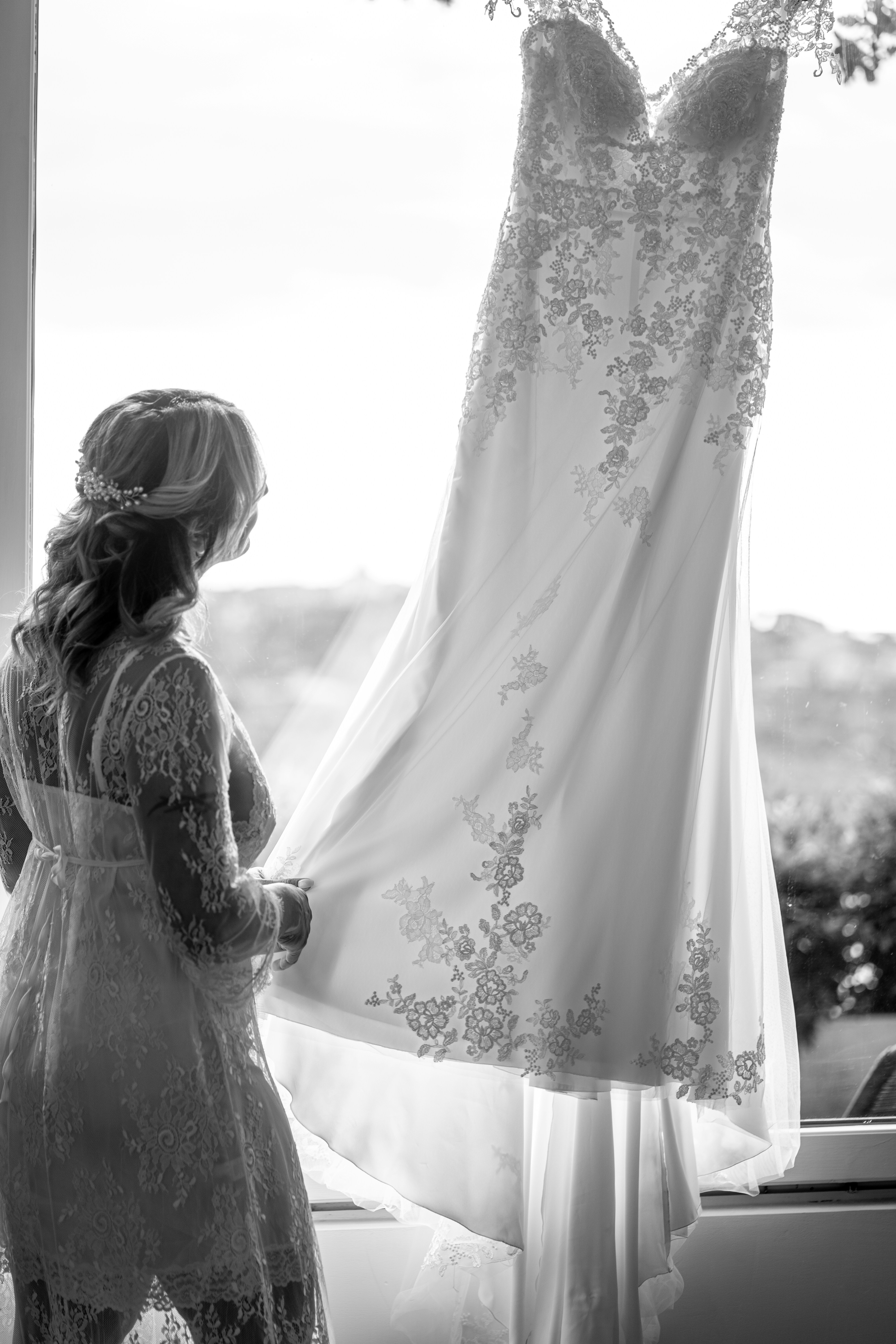 a woman looking at a wedding dress hanging in a window