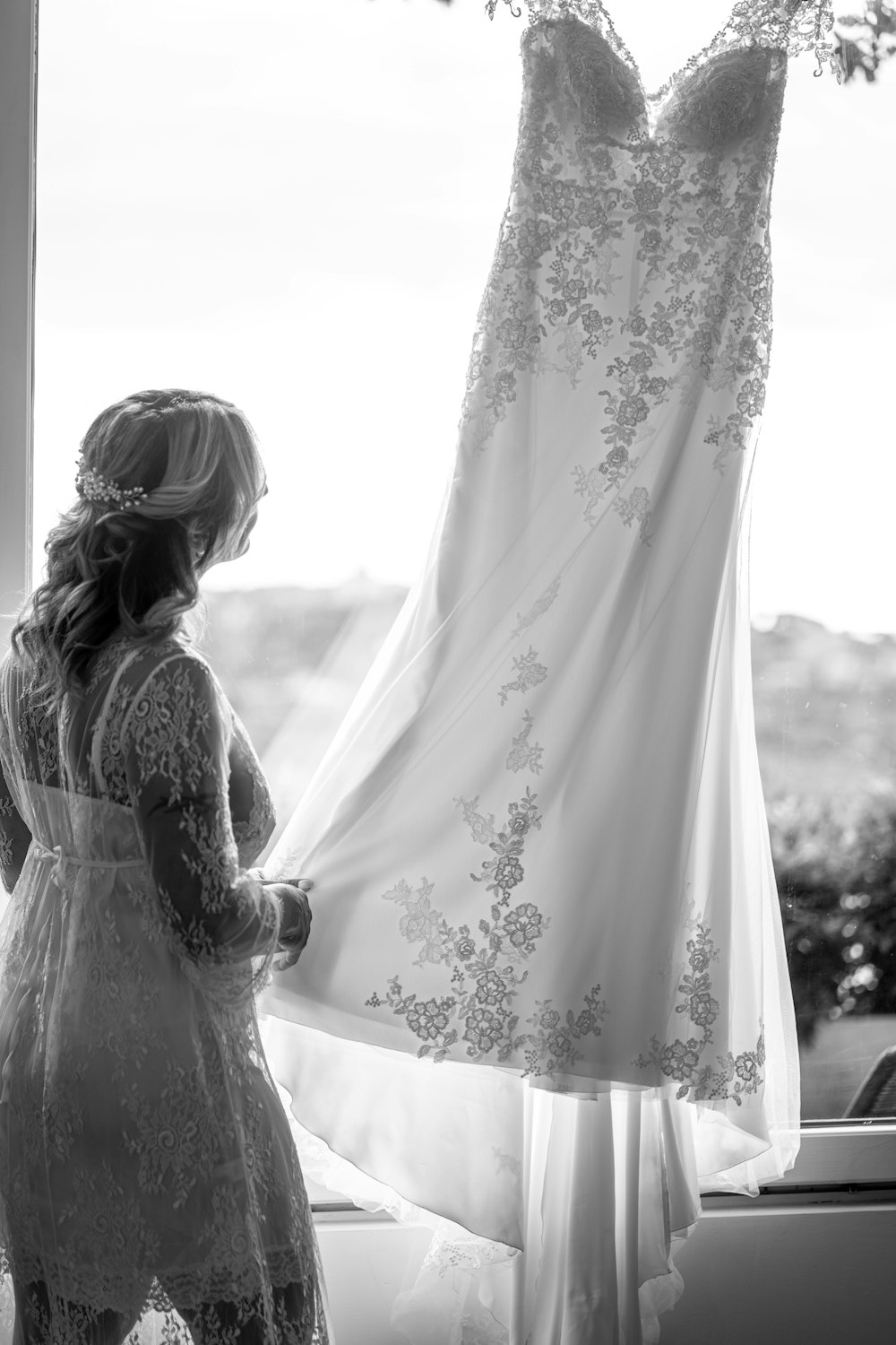 a woman looking at a wedding dress hanging in a window
