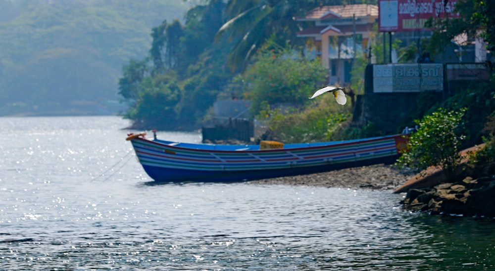 a blue boat floating on top of a lake next to a lush green hillside