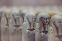Several ancient Egyptian statues resembling small, intricately carved figures are arranged in rows. The figures display traditional Egyptian style headdresses and are carved from stone.